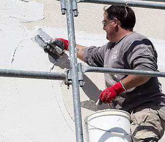 ouvrier Iso-Renov entrain d'étaler de l'enduit sur une façade