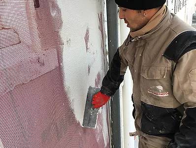 ouvrier Iso-Renov entrain d'étaler de l'enduit sur une trame en fibre de verre posée sur une façade