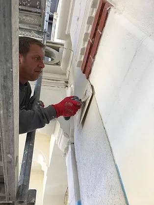 ouvrier Iso-Renov entrain d'étaler de l'enduit chaux aérienne sur une façade ancienne