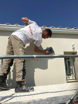 ouvrier Iso-Renov entrain d'étaler de l'enduit chaux aérienne sur un mur humide
